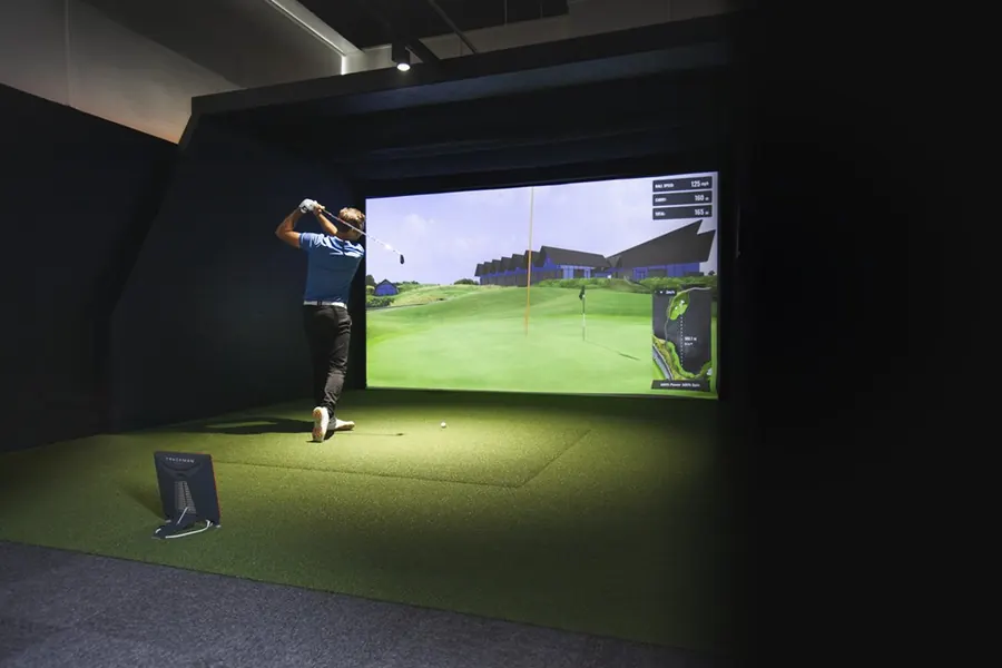 Golfer schlägt am Simulator auf einen virtuellen Golfplatz ab